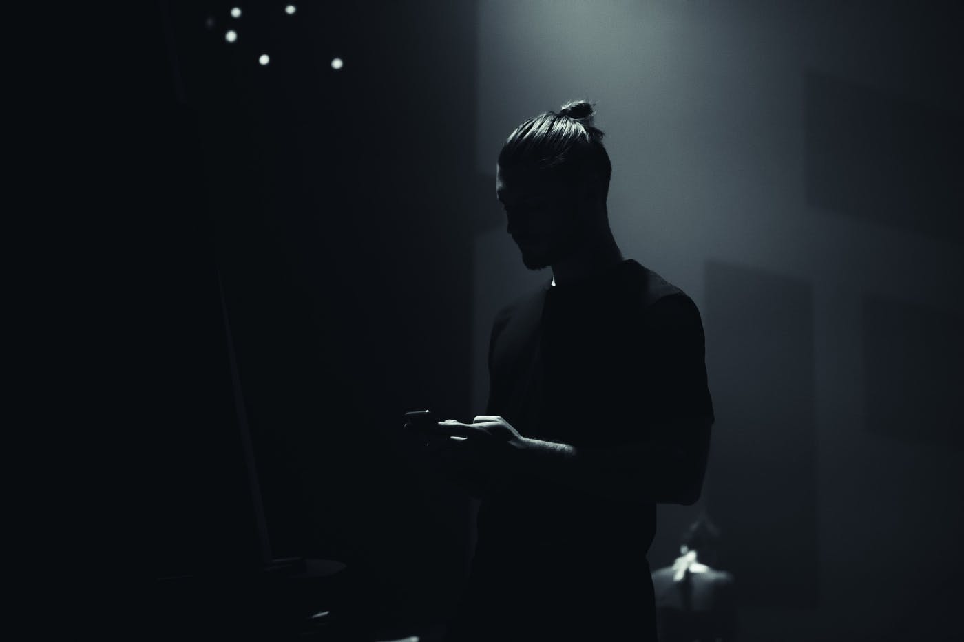 A man standing the shadows texting.