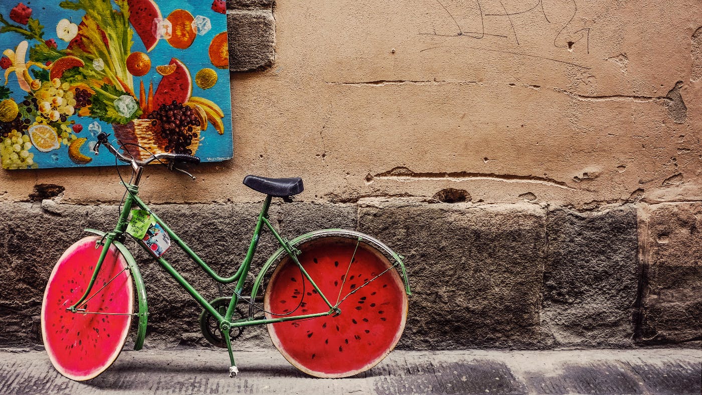 A wall with a canvas of fruit on it and a bicycle with watermelon slices for wheels