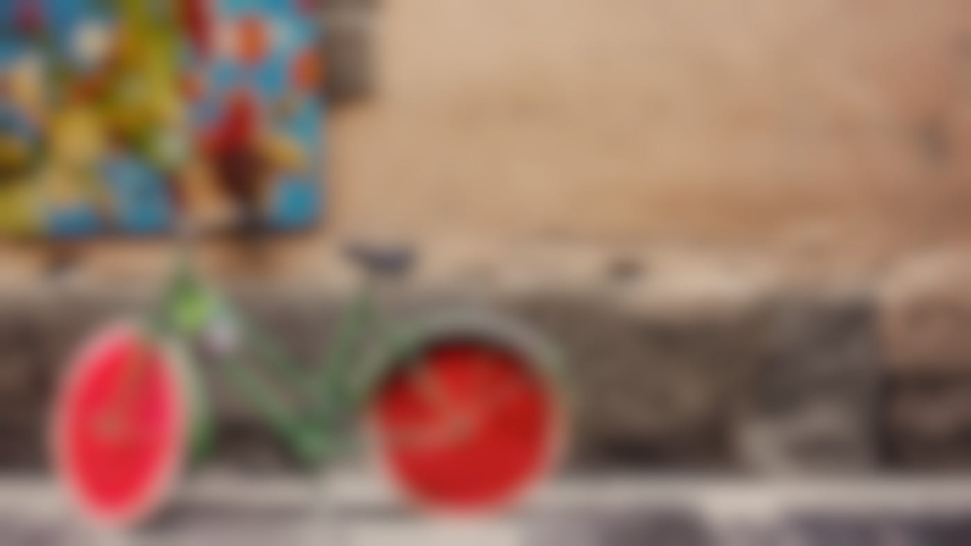 A wall with a canvas of fruit on it and a bicycle with watermelon slices for wheels