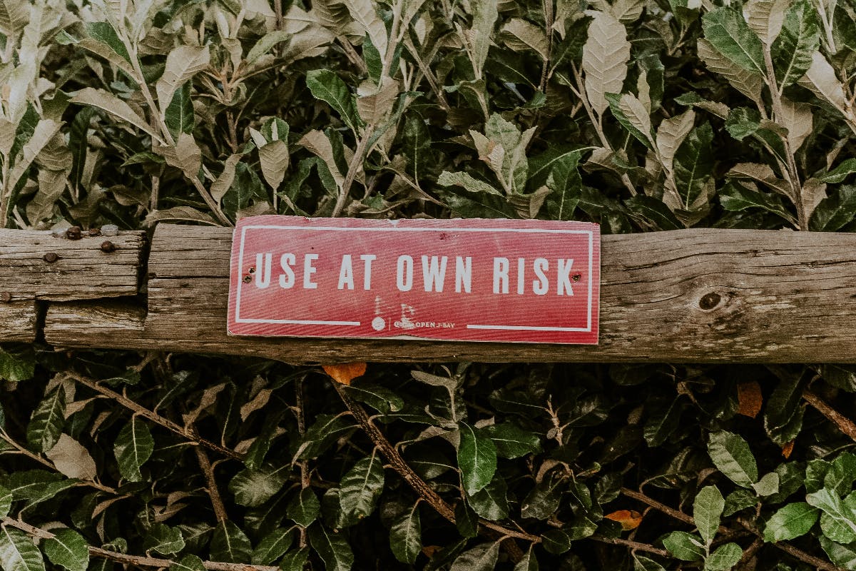 A wood fence pole in front of a bush with a red sign reading use at own risk