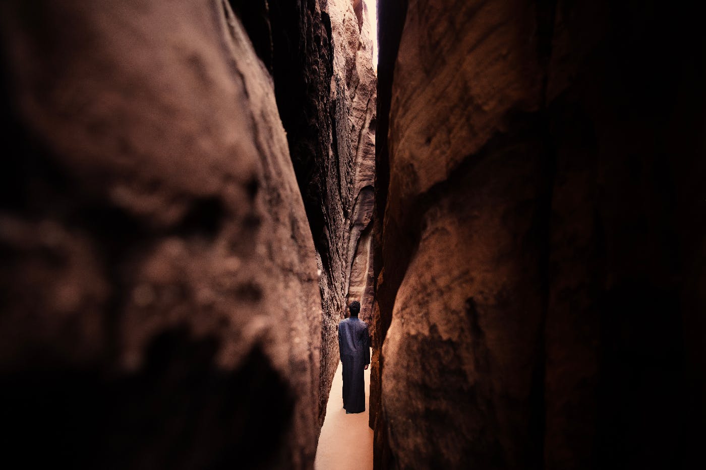 a woman in gray walking thru a tight crevasse
