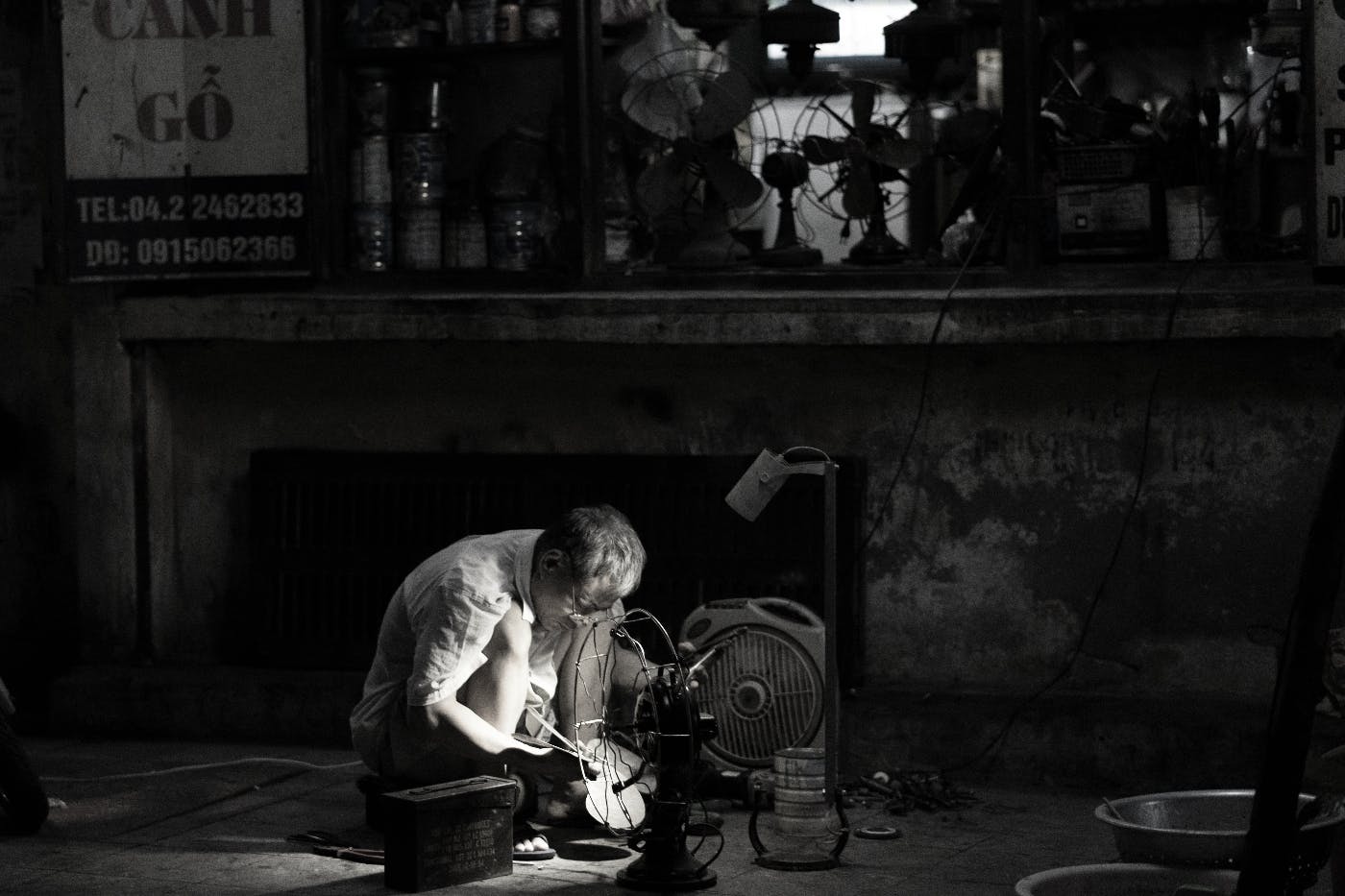 A man squatinfg on the floor in front of a fan making a violin.