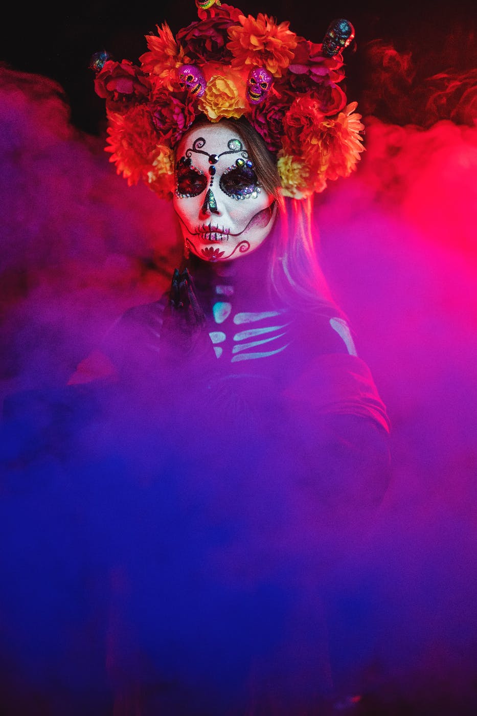 A woman in elaborate Day of the Dead make up standing in blue and red smoke