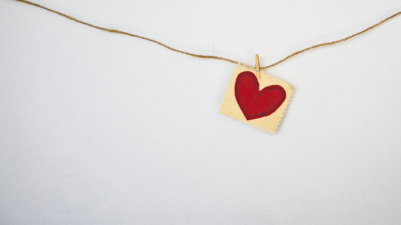 A small red felt heart sewn to a yellow square of muslin clipped to a twine line with a clothespin