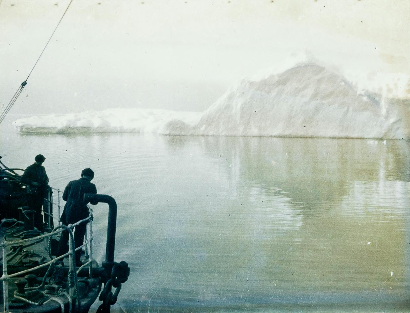 black and white of two men on a boat approaching an iceberg