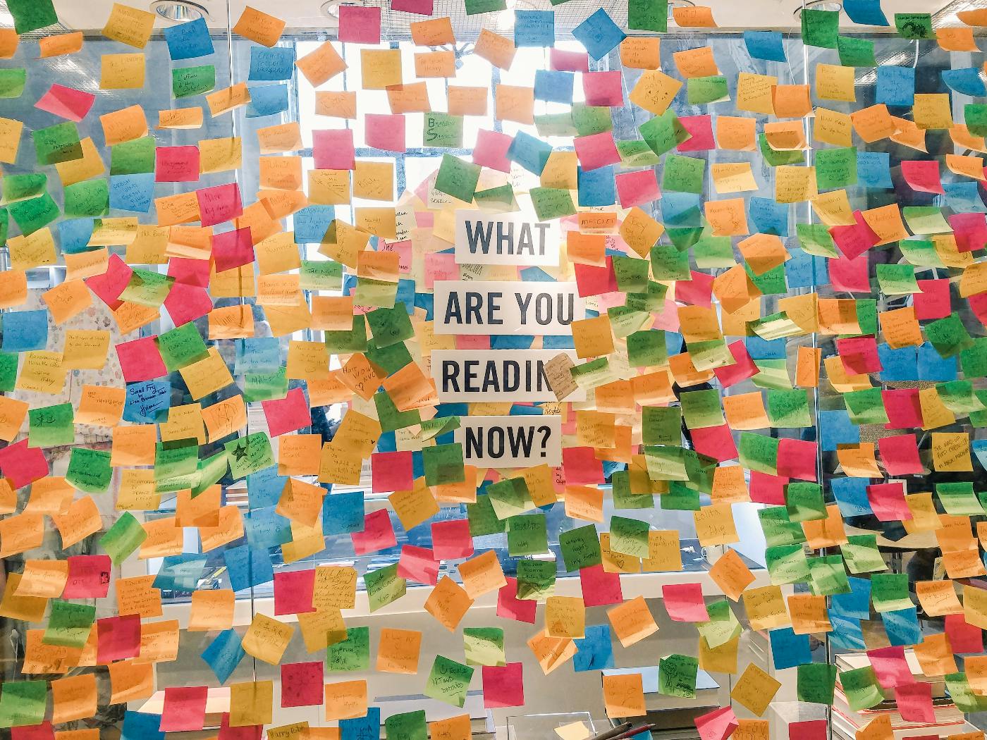 A wall covered with post-its and the words Whar are you reading now?