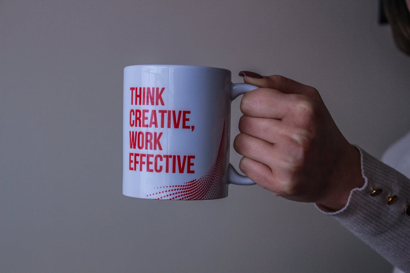 A woman holding a coffee mug that reads Think Creative, Work Effective