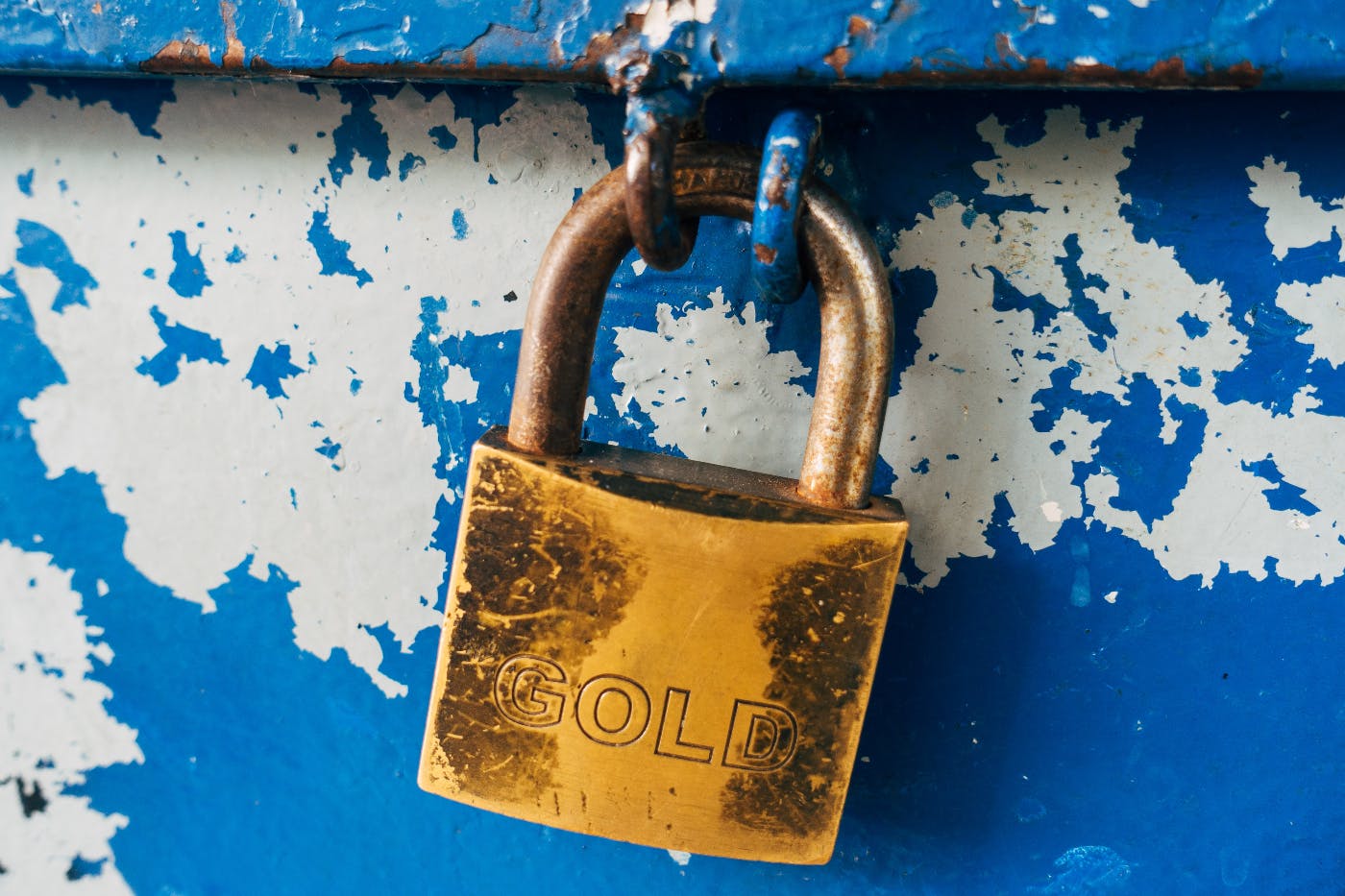 A gold padlock attaced to a chipped blue container