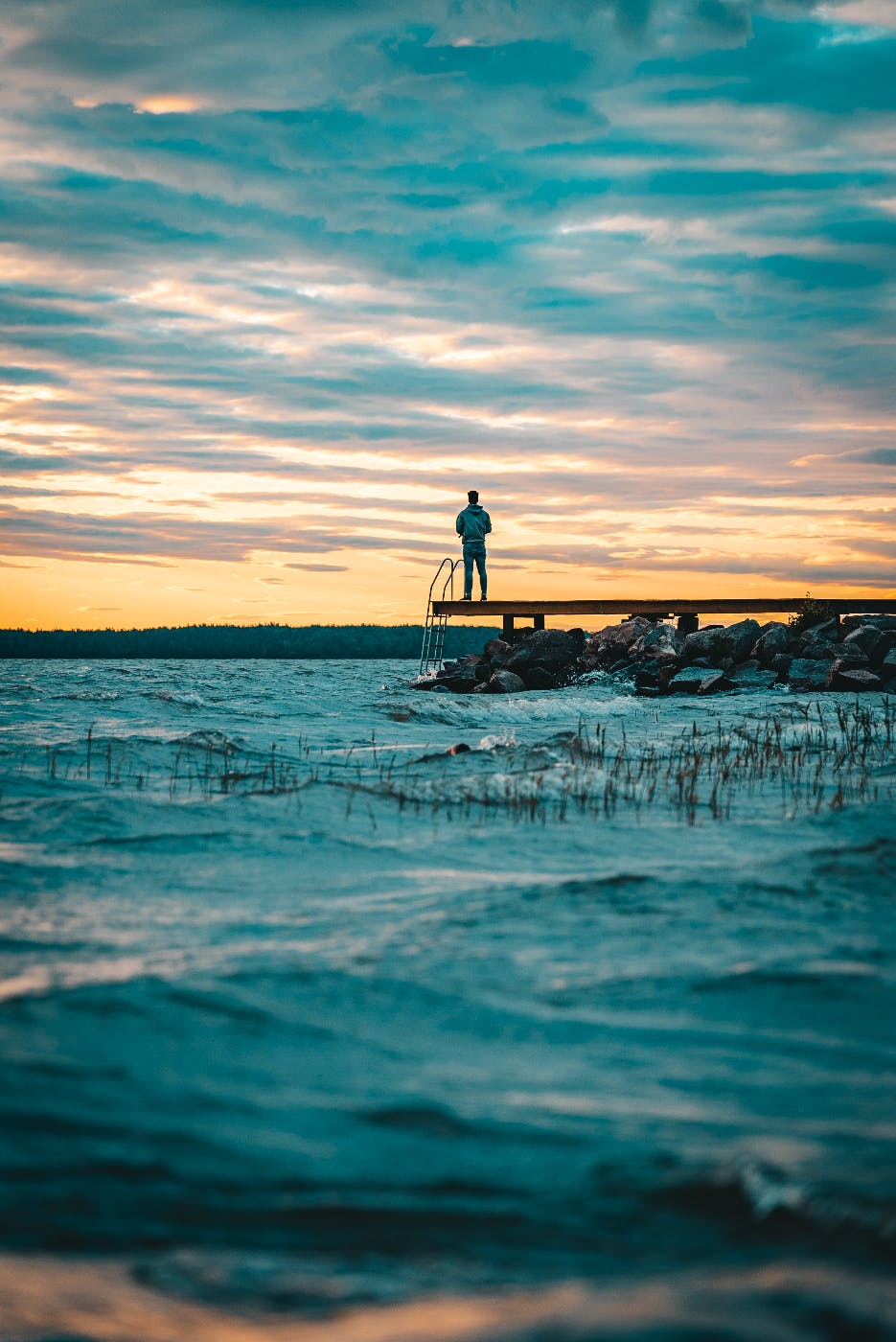 A man standing on a dock stretching out into a topaz blue ocean