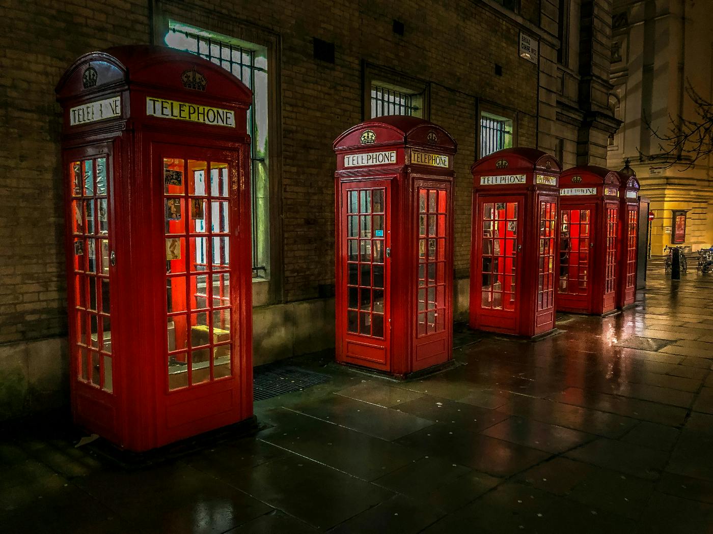 a line of five red British call boxes on a rainy street