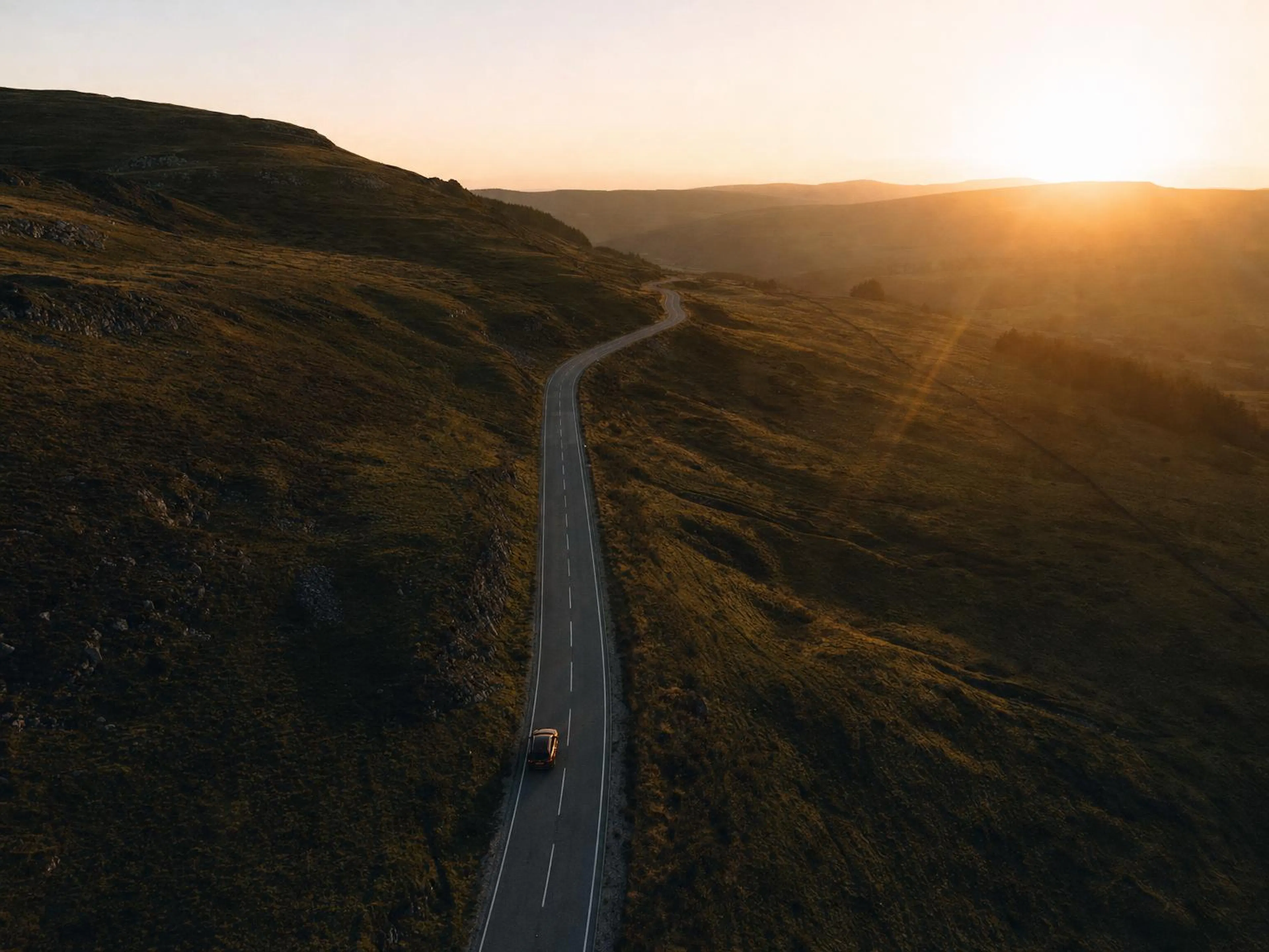 Aerial view at golden hour of a winding road through green English hills
