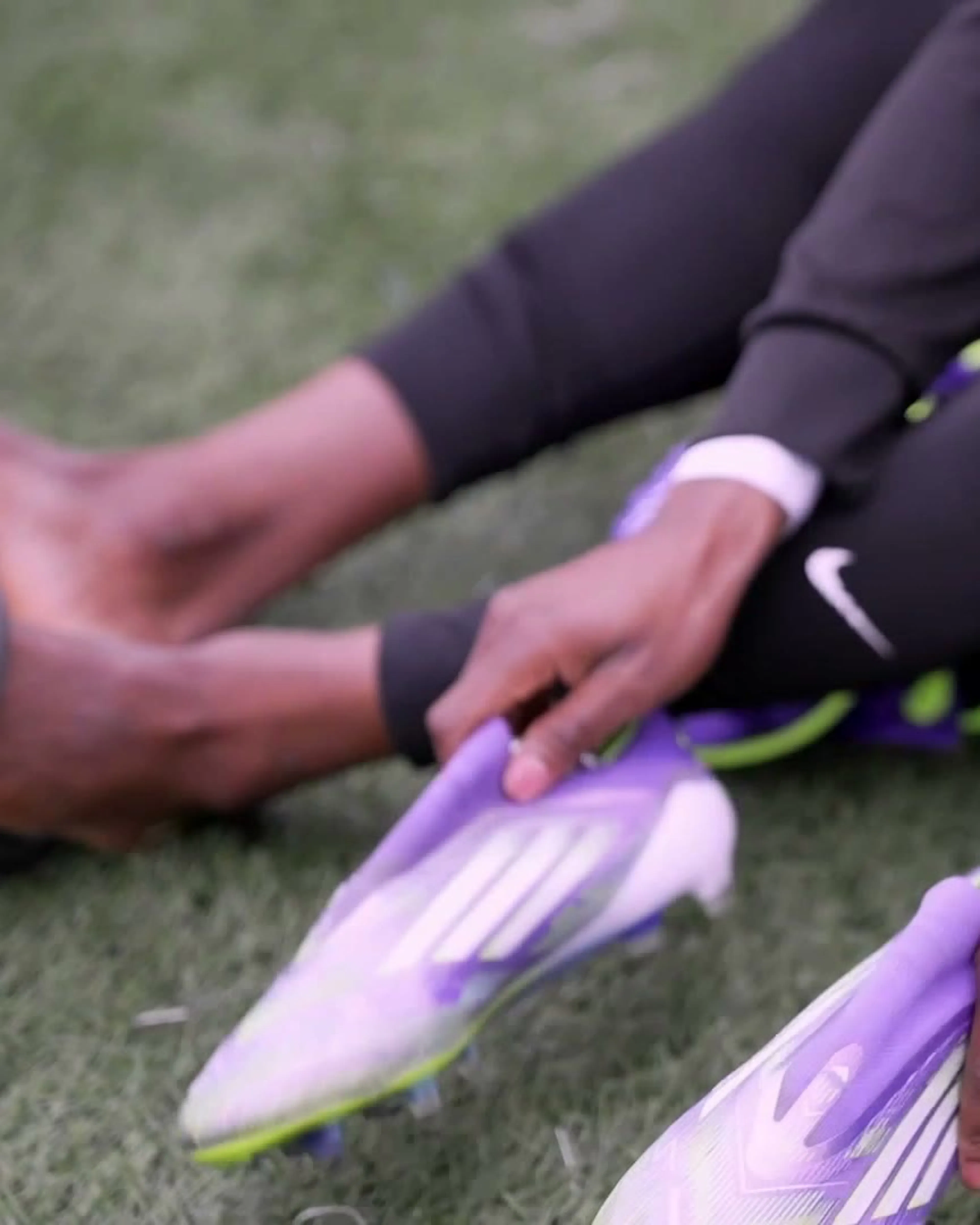 Close-up of a player pulling on lilac football boots on the pitch side