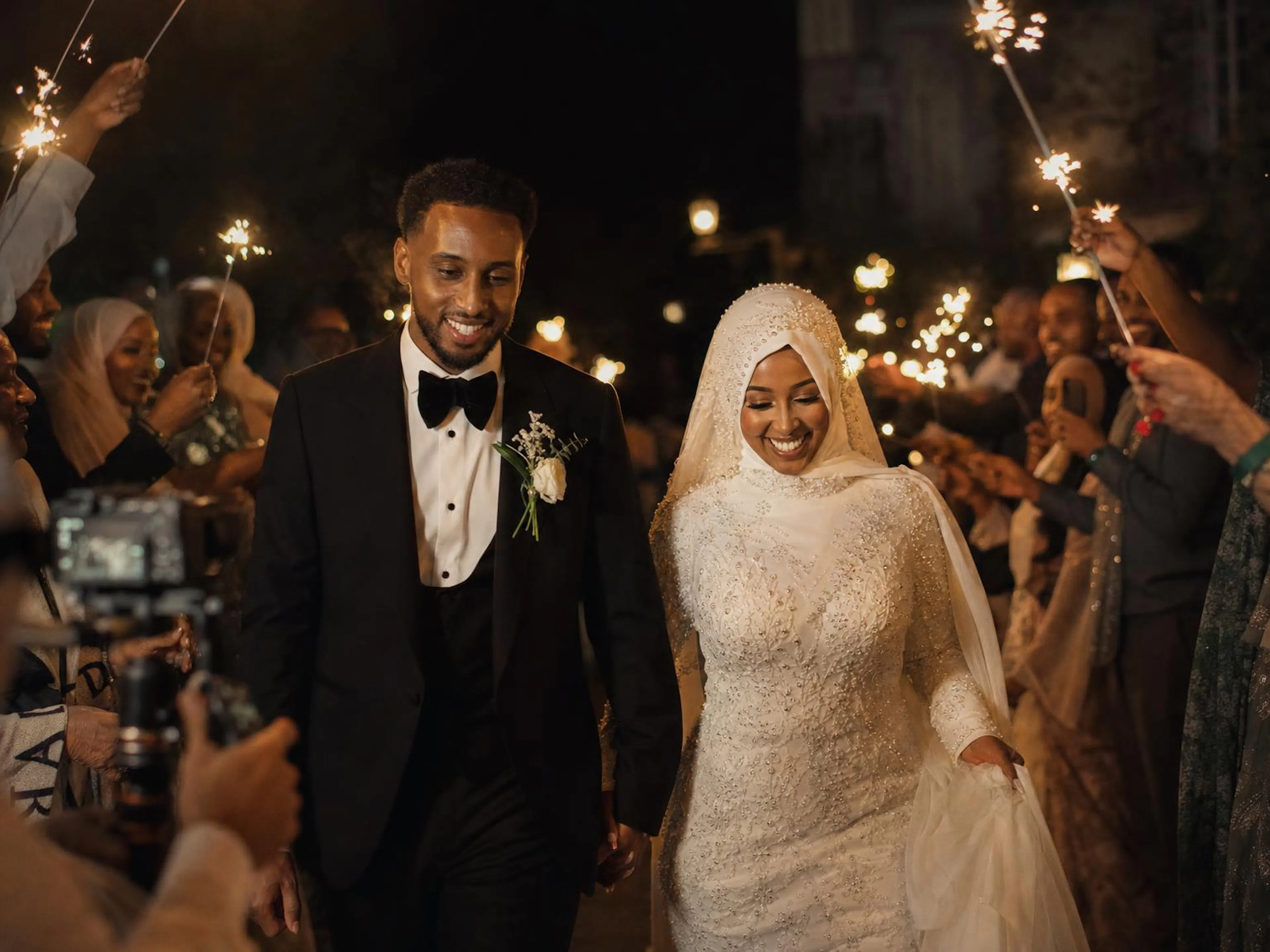 A bride and groom walking through guests holding sparklers at their wedding reception