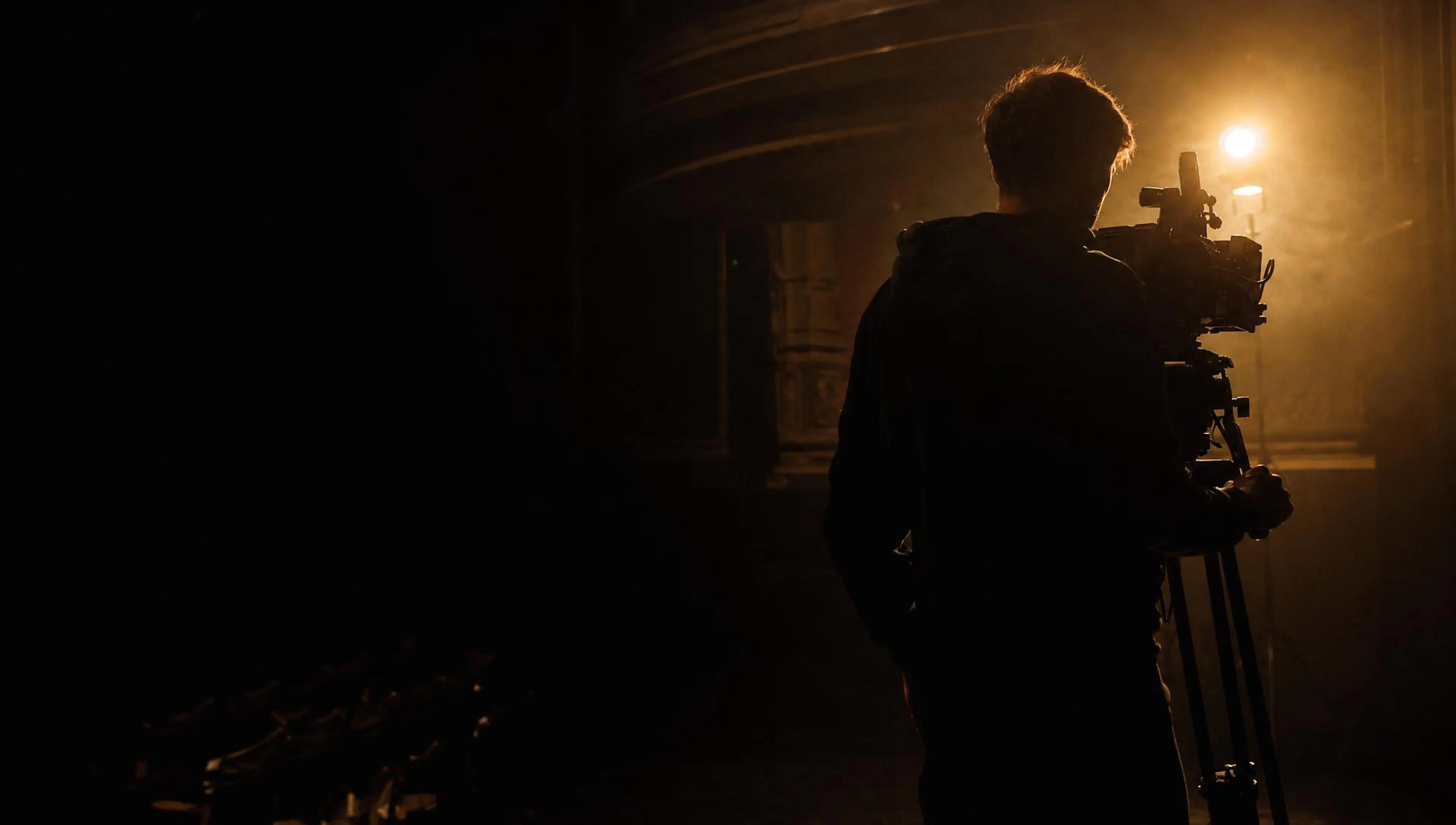 A camera operator silhouetted against a warm stage light in an empty theatre