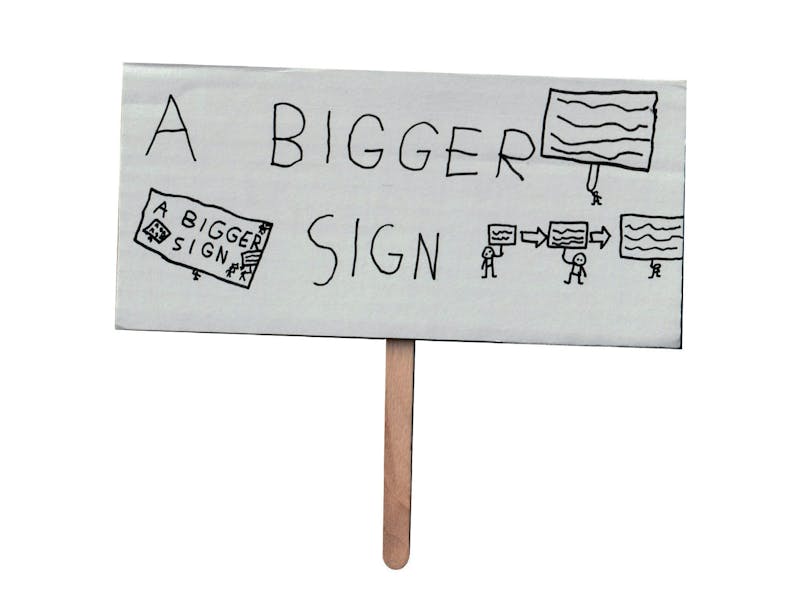 A tiny protest placard made of an envelope stuck to an ice lolly stick. on the placard it says A BIGGER SIGN next to a diagram of stick men holding progressively larger placards. 