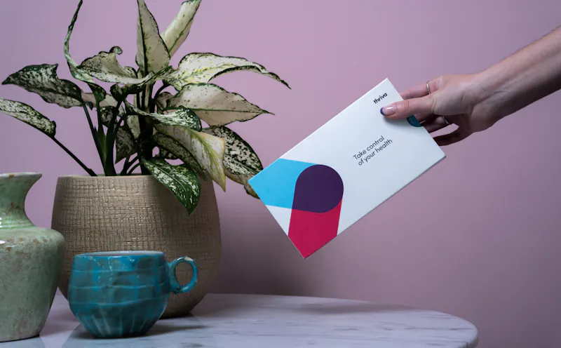 Hand placing Thriva test kit on marble table with plants
