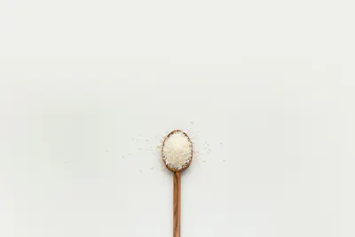 Grains of salt on wooden spoon on white background