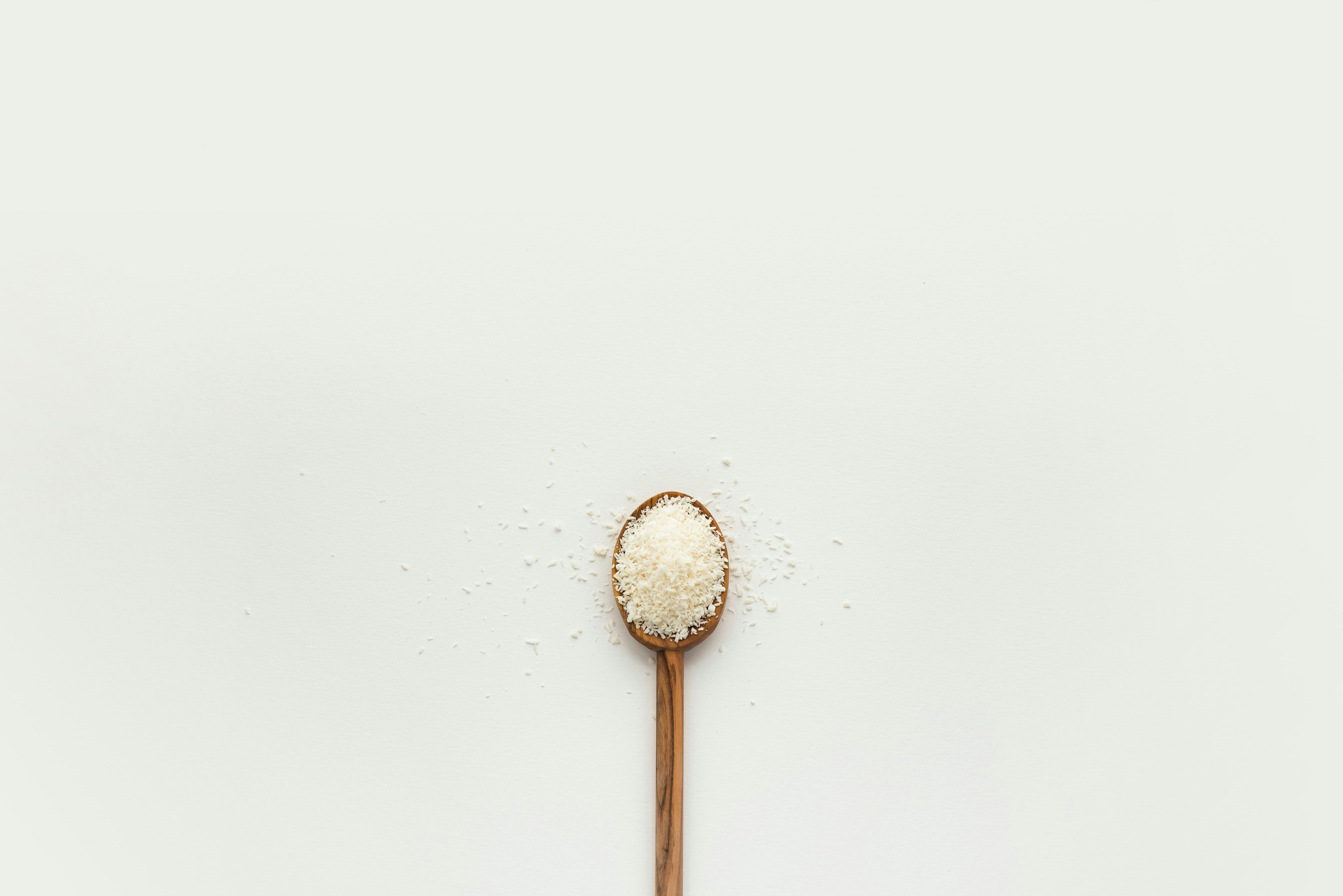 Grains of salt on wooden spoon on white background