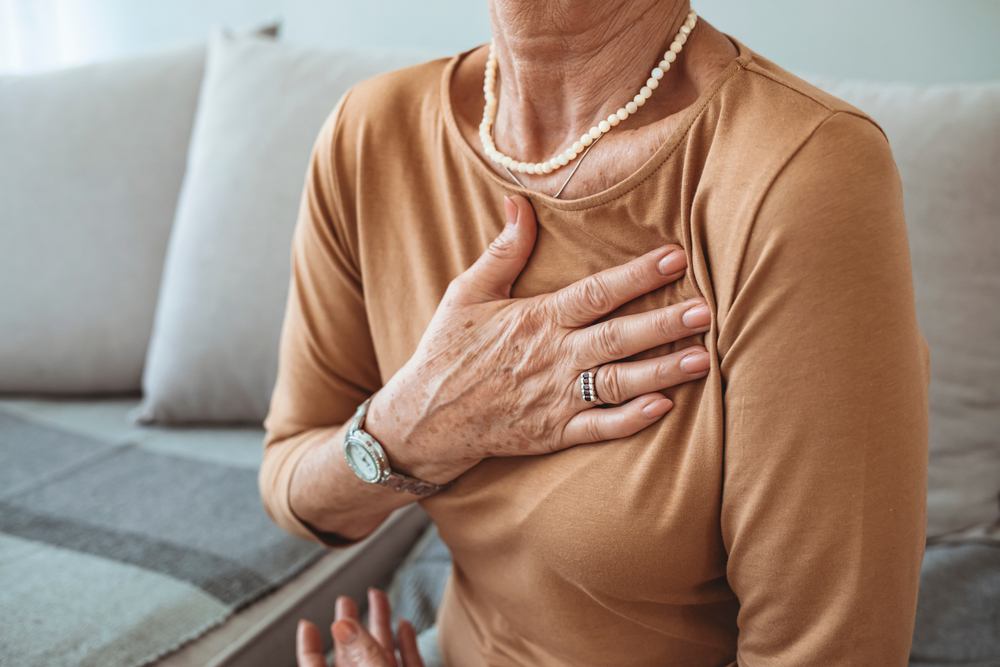 Woman with hand to her chest, sitting on sofa, wearing jewellery