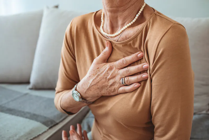 Woman with hand to her chest, sitting on sofa, wearing jewellery