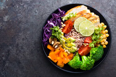 Black bowl filled with nutritious vegetables, fruits, chicken and more