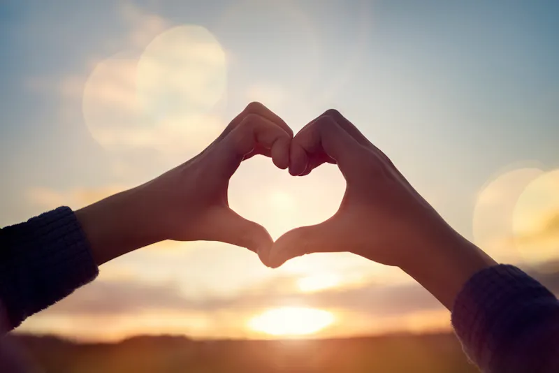 Hands held into heart shape in front of sunrise