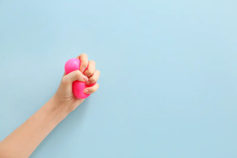 Hand squeezing pink stress ball on blue background