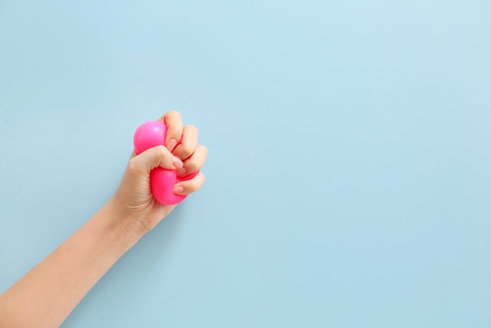 Hand squeezing pink stress ball on blue background