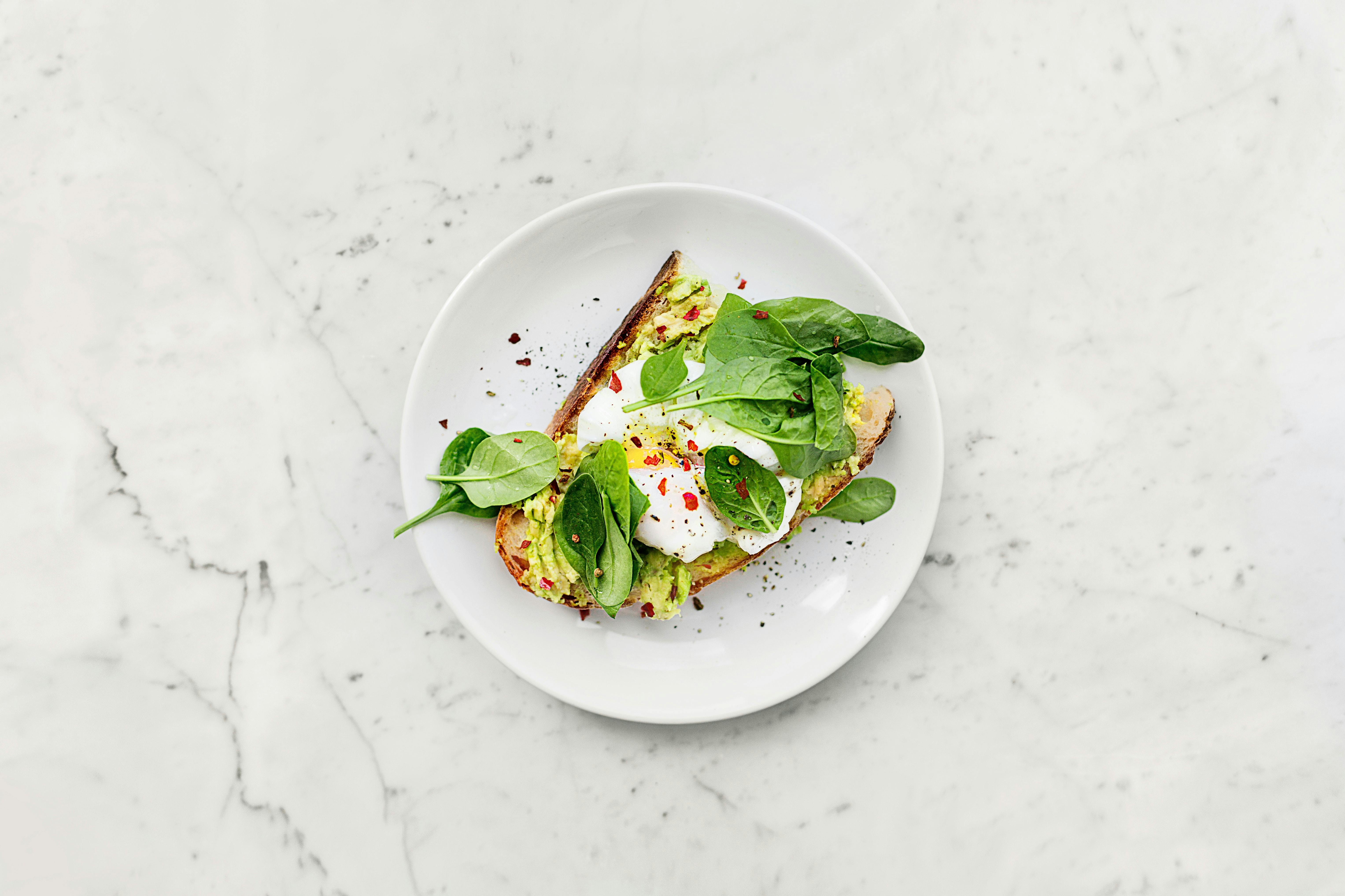 Avocado on toast with egg and spinach on white plate on marble background