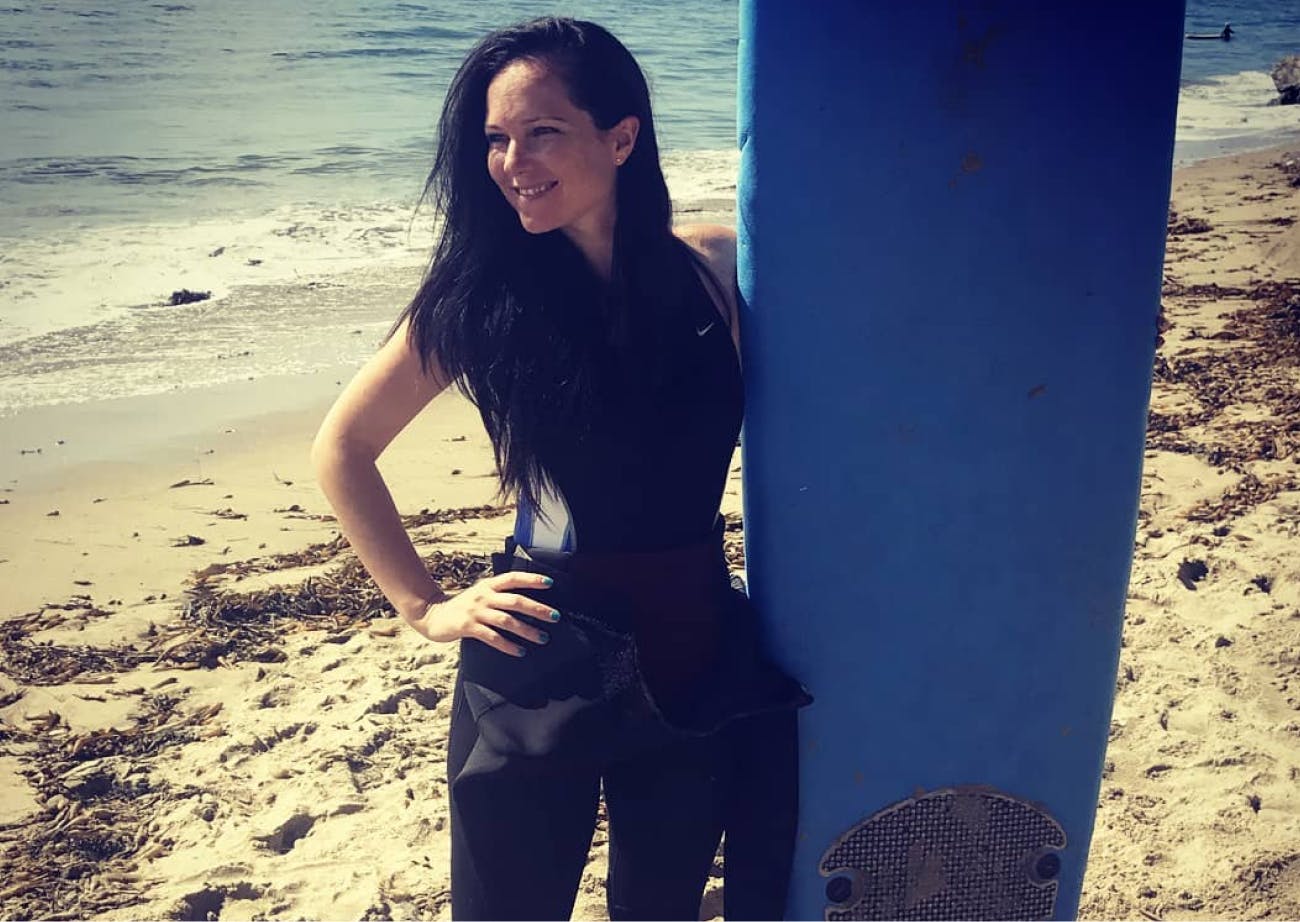 Naomi holding a surfboard at the beach