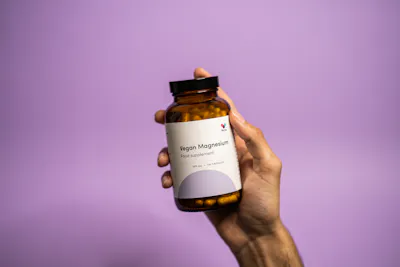 Thriva's vegan magnesium supplements pot in hand on purple background