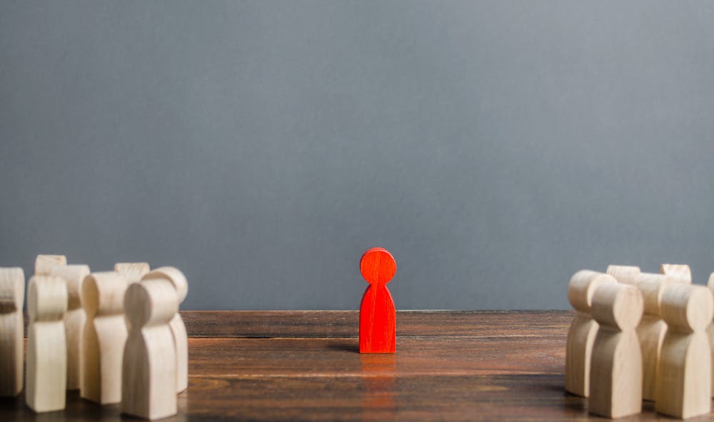 Red figurine standing on its own away from other figurines on wooden table