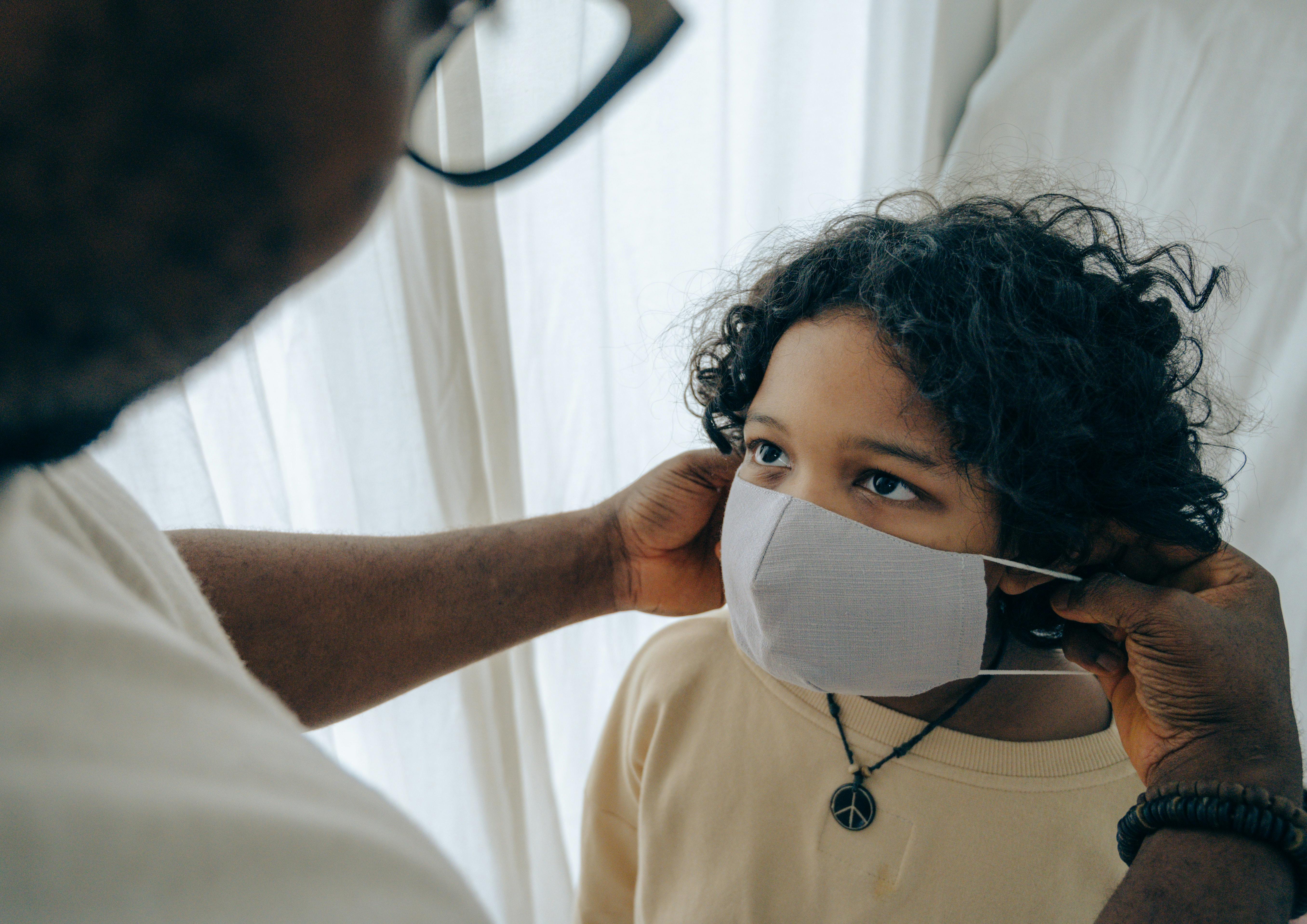 Man placing a medical face mask onto a child's face
