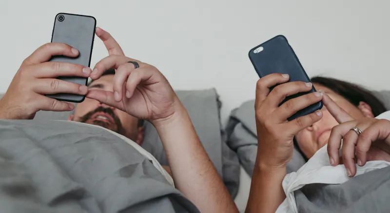 Two people in bed scrolling on their phones.