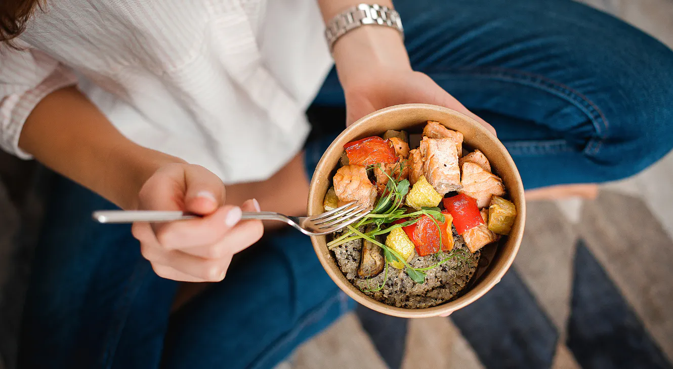 A woman eating a salad with vegetables and salmon.
