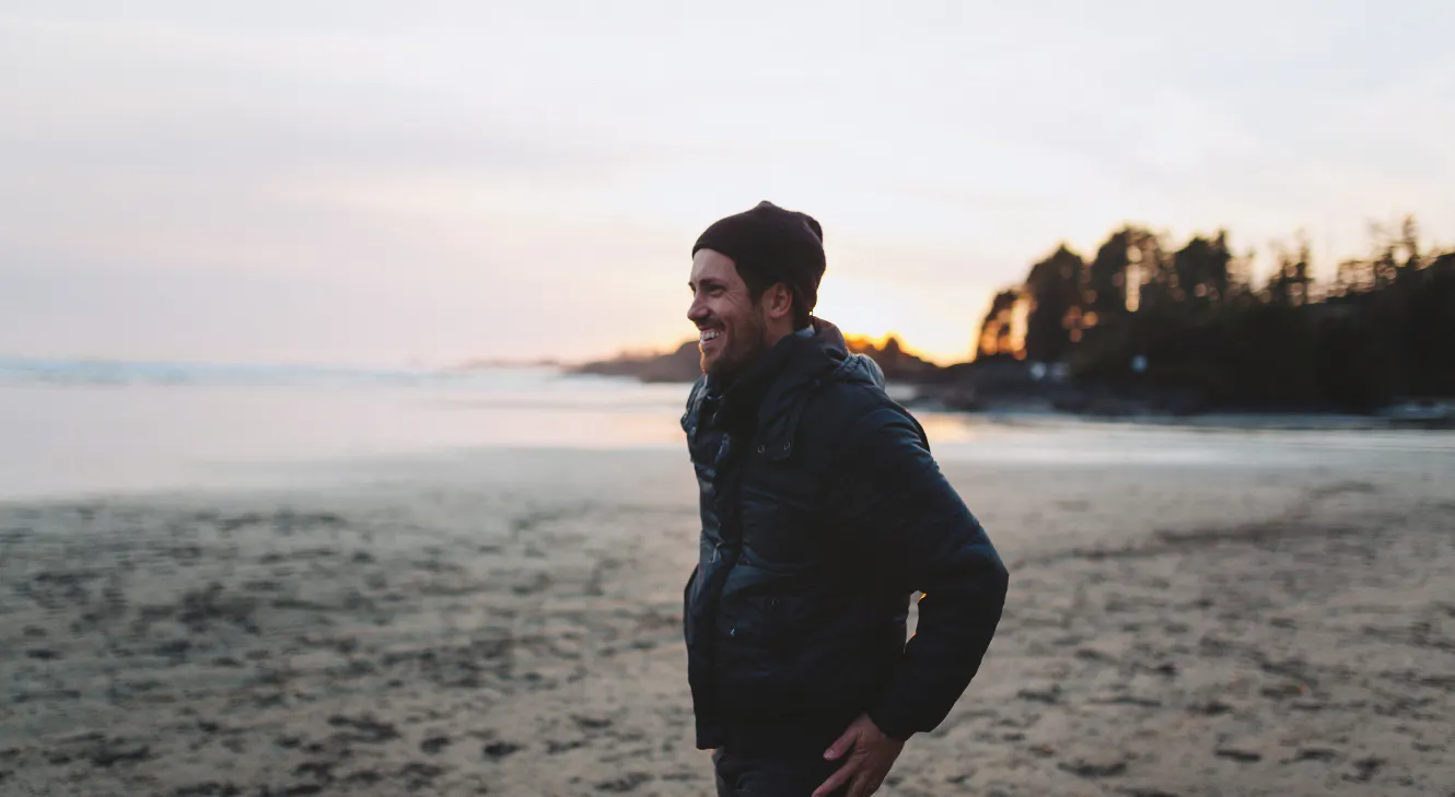 A man smiling and walking along a beach