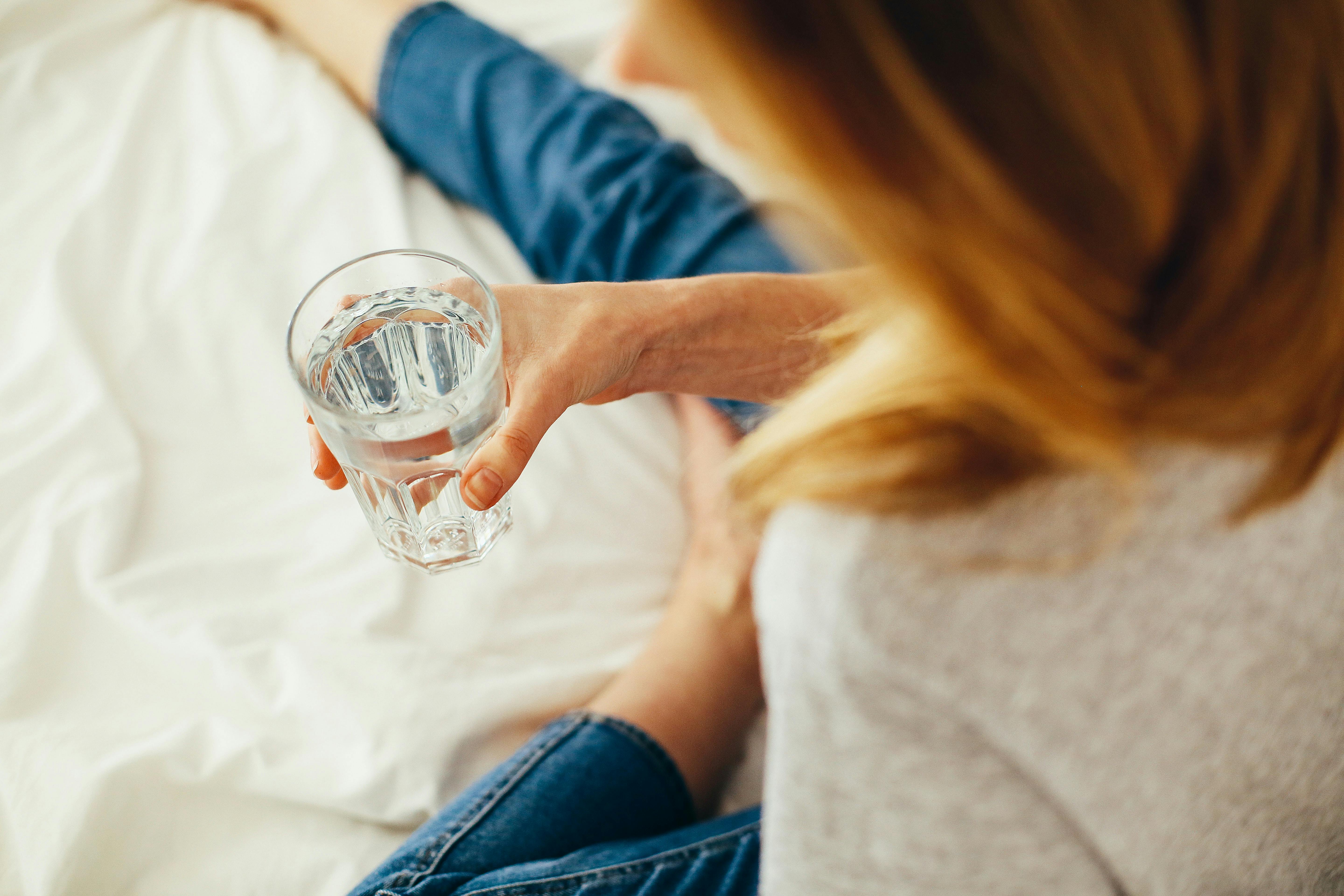 Woman sat on bed with glass of water