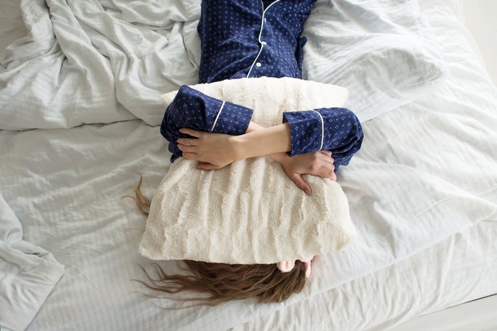 Sleepy woman lying in bed covering her face with a pillow