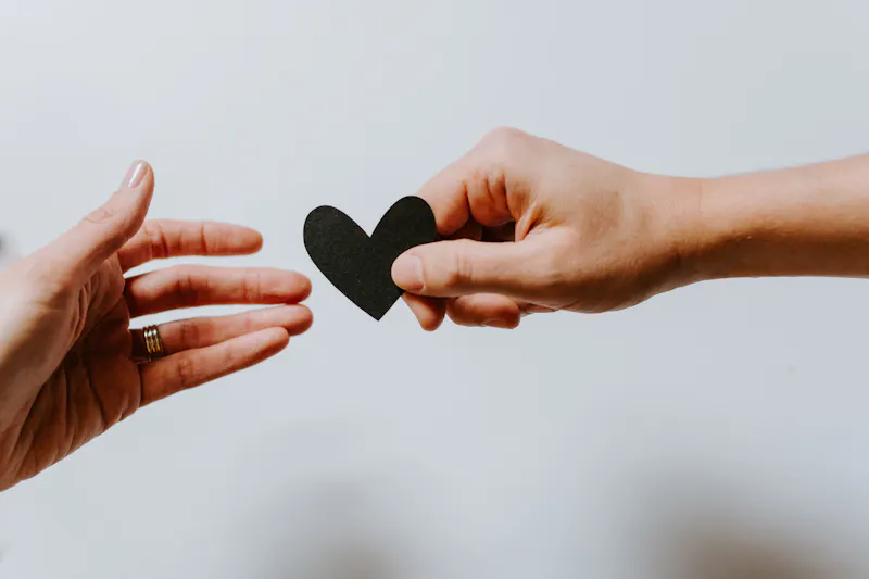 Hands passing black paper heart cut out