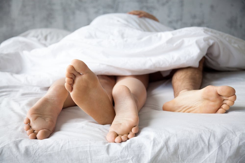 Two pairs of feet sticking out the end of a bed