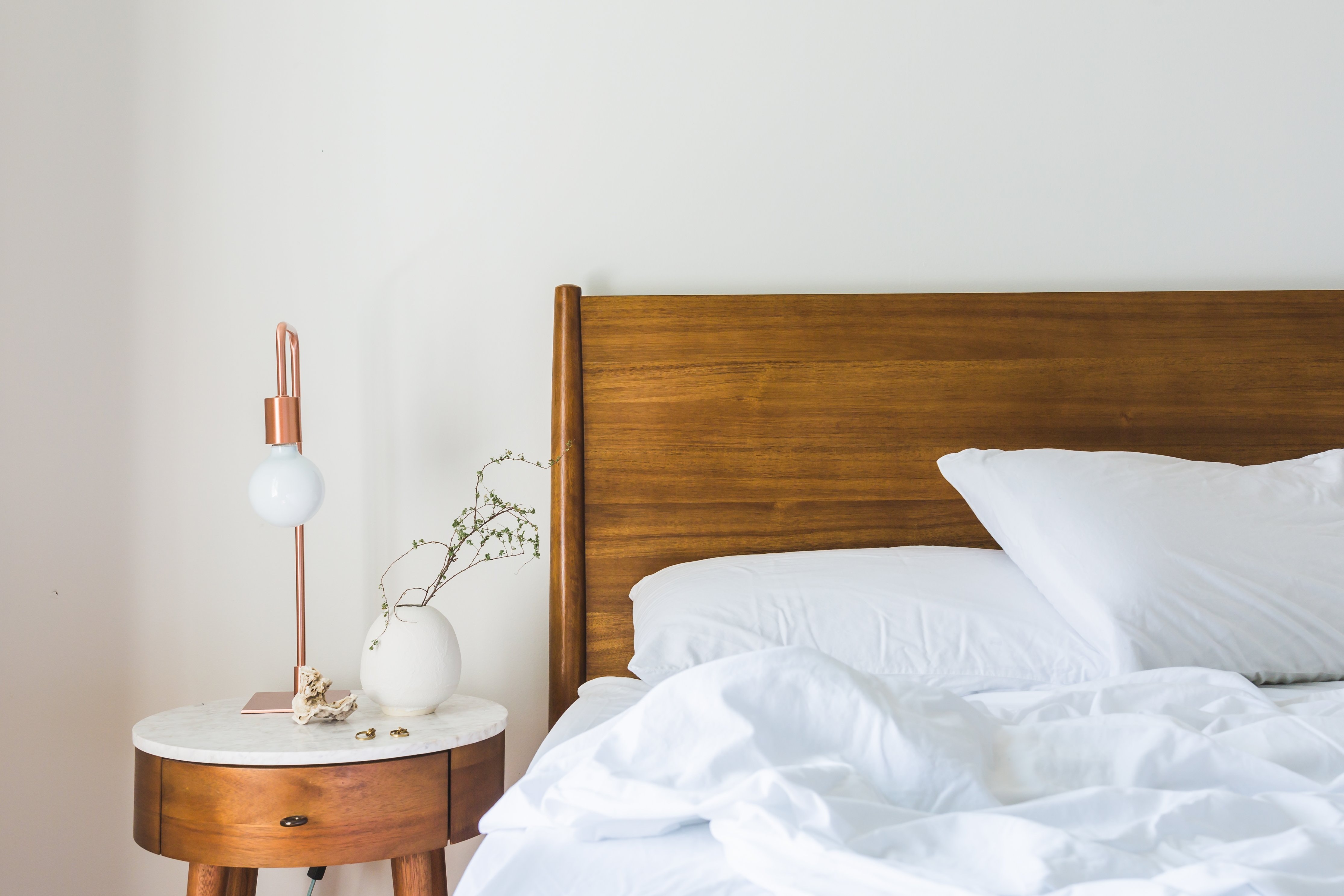 Corner of wooden bed with white pillows and bedside table