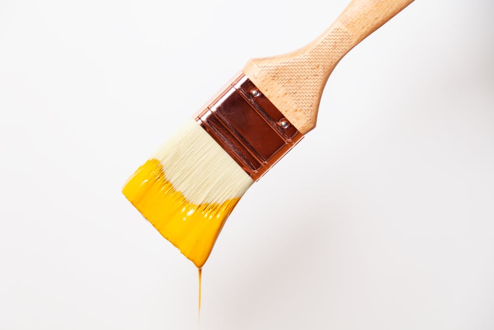 Yellow paint dripping from paint brush on white background