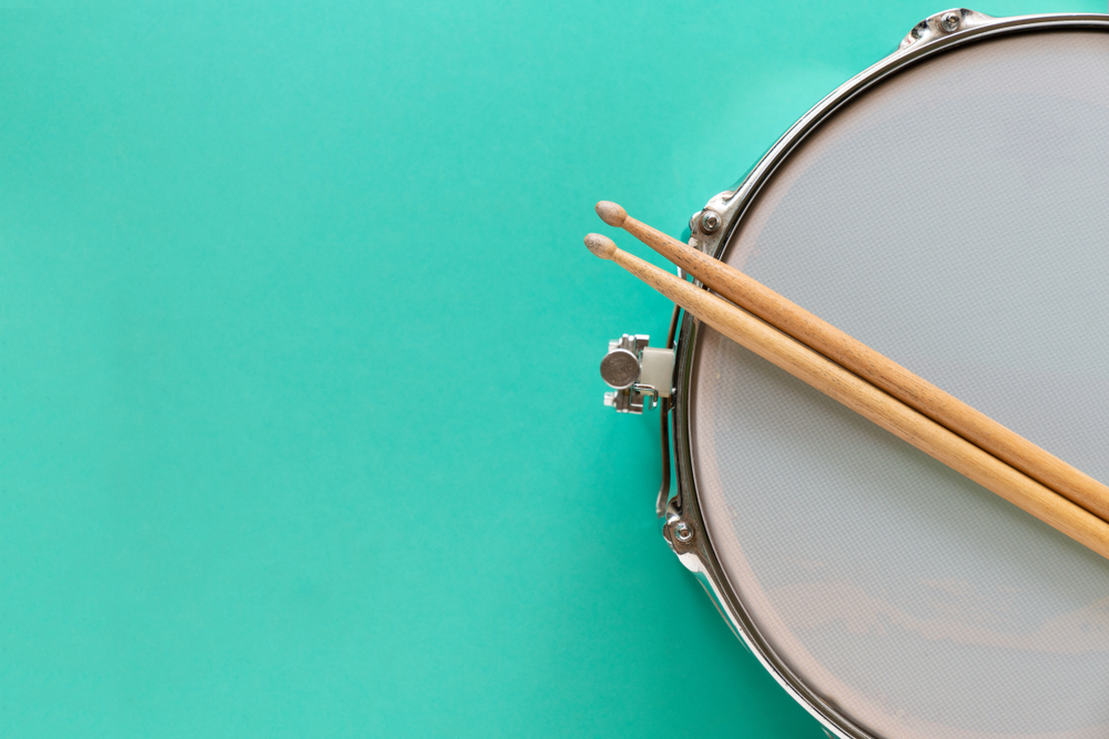 Drumsticks resting on drum, turquoise background