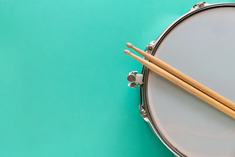 Drumsticks resting on drum, turquoise background