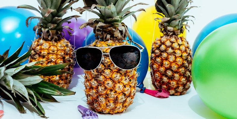 Multiple balloons in different colors, pineapples wearing party hats, and sunglasses.