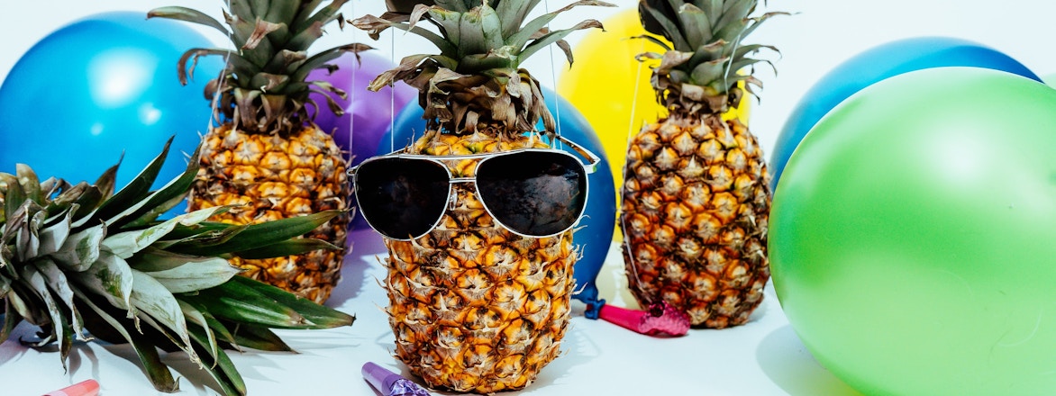 Multiple balloons in different colors, pineapples wearing party hats, and sunglasses.