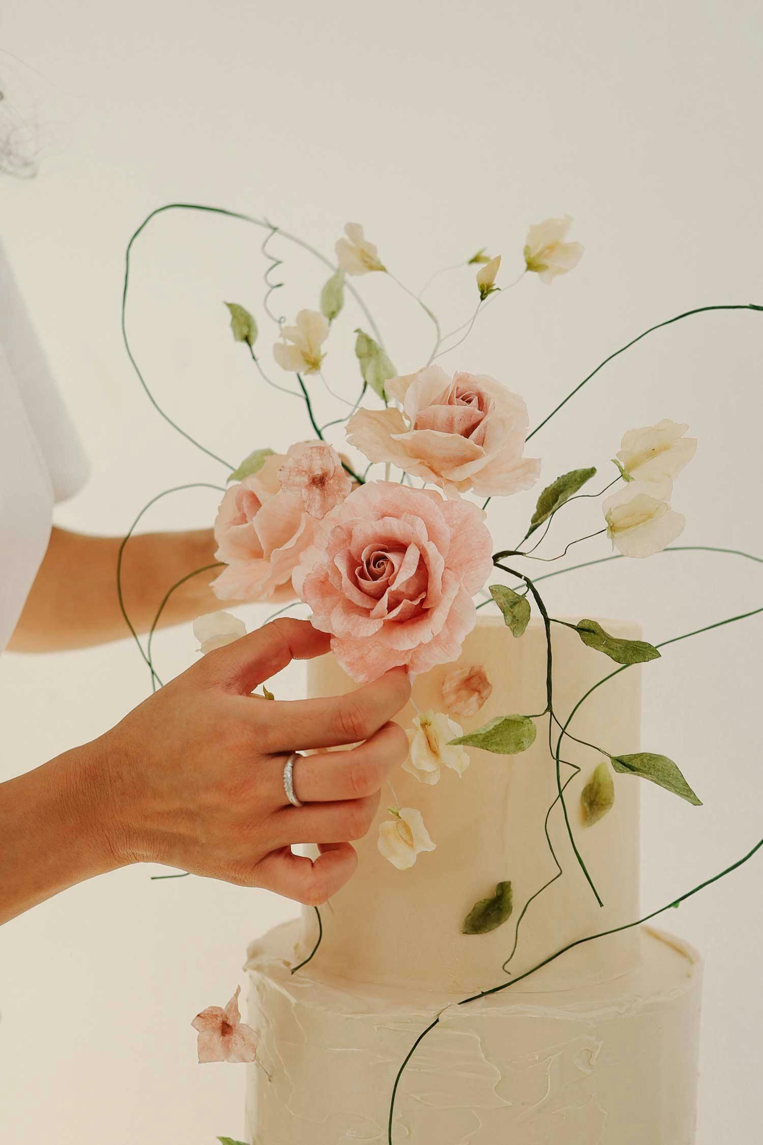 A hand rearranging the flowers of a wedding cake