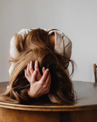 femme avec la tête dans les mains sur une table ronde en bois