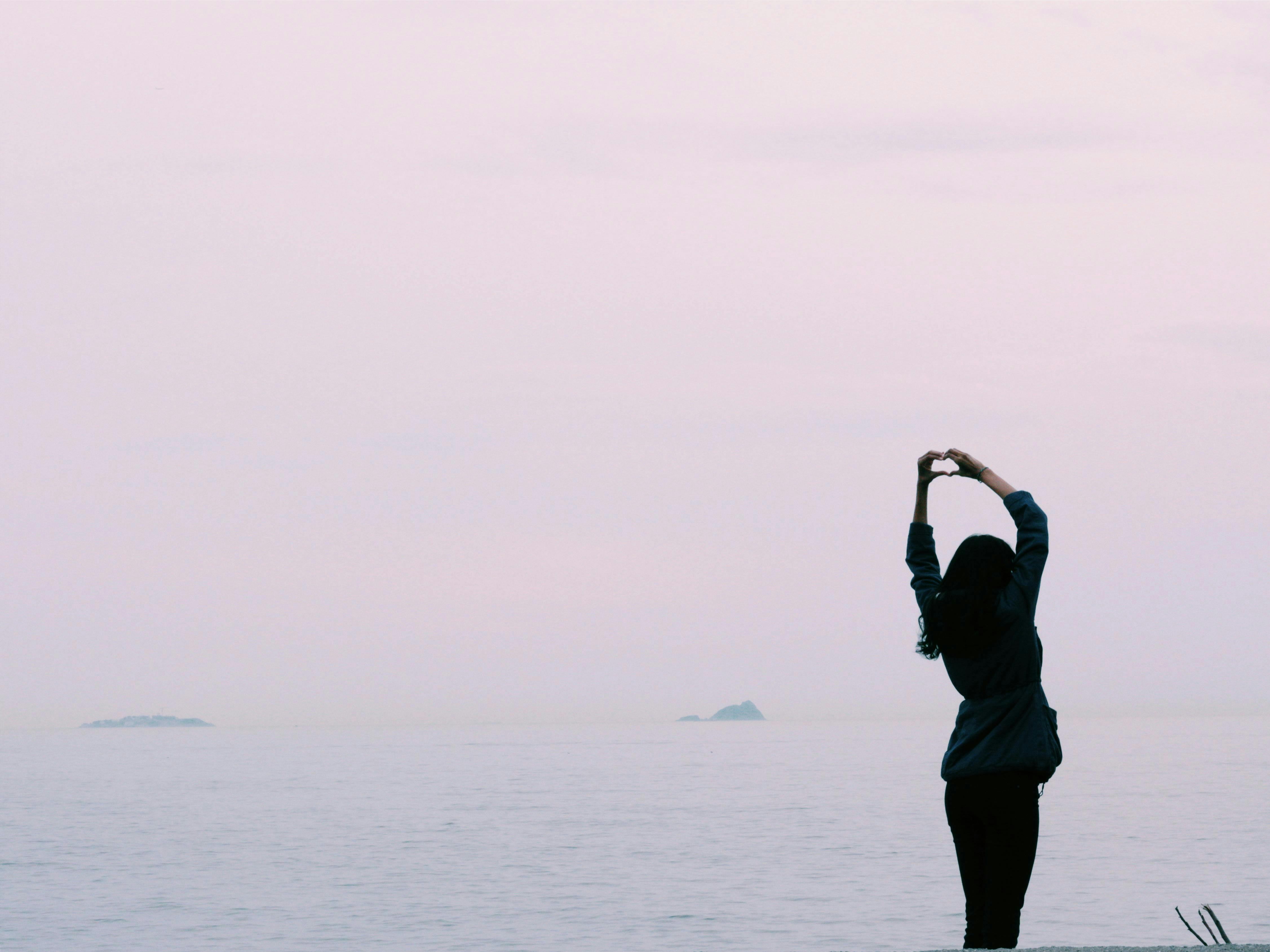 femme au bord de l'eau faisant un coeur avec ses mains