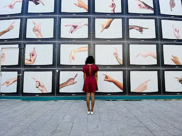 femme en robe rouge de dos devant des écrans de tv avec des mains